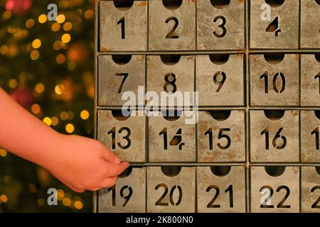 Metallischer Adventskalender im Vintage-Stil und Kinderhand. Weihnachtstraditionen und -Symbole. Geschenke und Überraschungen für Neujahr Stockfoto