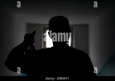 Silhouette eines Mannes mit einer Flasche Bier. Mann im Dunkeln zeigt Alkohol. Mann vor der Türe. Unbekannte Person. Trunkenheit in der Gesellschaft. Stockfoto