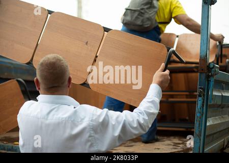 Der Lader hält den Laden. Der Mann stellt eine Bank in den LKW. Demontage von Gartenmöbeln. Person, die schweres Objekt hält. Bürotransport. Stockfoto