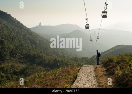 Ein Wanderer beobachtet die Seilbahn, die Touristen zum Dorf Ngong Ping und zum Big Buddha bringt, sichtbar im Dunst am Horizont, Lantau Island, Hongkong Stockfoto