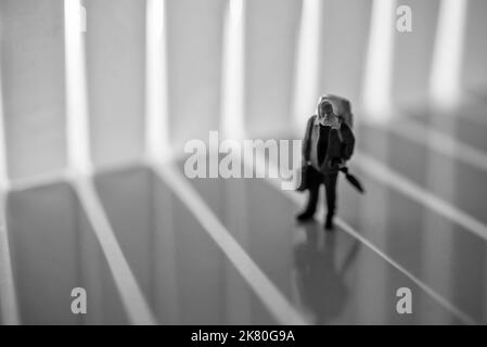 Miniatur-Spielzeug-Studio eingerichtet - ein alter Mann mit Rucksack und Regenschirm zu Fuß bei Sonnenaufgang oder Sonnenuntergang. Rauschen für dramatische Effekte hinzugefügt. Stockfoto