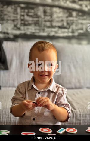 Porträt eines niedlichen kleinen Jungen, der mit Buchstaben und Zahlen auf einem Tisch spielt Stockfoto