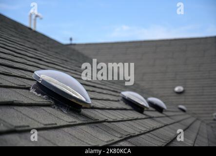 Kuppelförmiges Sonnenröhren-Oberlicht auf Asphalt-Schindeldach Stockfoto