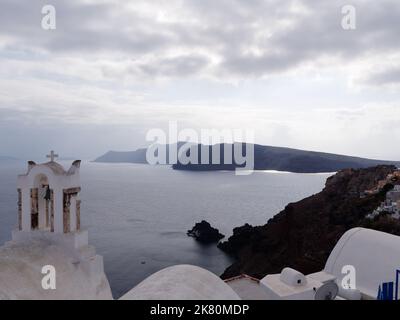 Blick auf die Stadt Oia und Caldera vom Kirchendach mit Kirchenglocken im Vordergrund. Griechische Kykladen-Insel Santorin in der Ägäis. Stockfoto