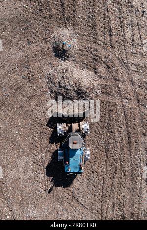 Luftaufnahme direkt über einer Bulldozer-Maschine, die Abfall und Hausmüll auf einer großen Mülldeponie mit Kopierfläche bewegt Stockfoto