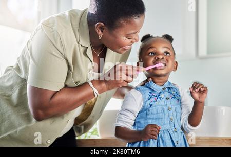 Eine Mutter putzt ihre kleinen Töchter zu Hause im Badezimmer mit den Zähnen. Stockfoto