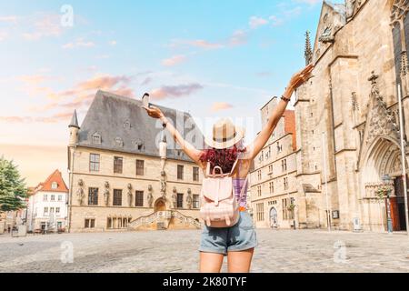 Fröhliche Frau mit Rucksack, die das Panorama des Rathauses rathaus und des Marktplatzes der Altstadt von Osnabrück in Deutschland genießt Stockfoto