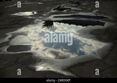 Große Pfütze in der Straße. Spiegelung des Himmels in der Pfütze. Wasser auf Asphalt. Große Pfützen nach Regen. Stockfoto