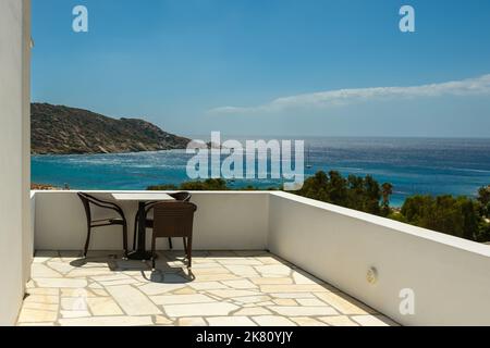 Ein Balkon mit Stühlen und einem Tisch mit Blick auf den berühmten Mylopotas Strand in iOS Griechenland Stockfoto