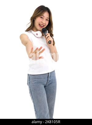 Junge asiatische Frau im weißen T-Shirt und jean stehen lächelnd mit Kopfhörern am Hals und singen mit Mikrofon. Porträt auf weißem Hintergrund mit studi