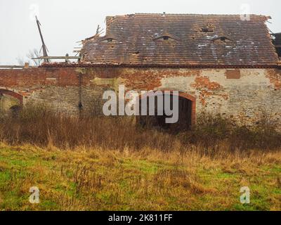 Alte verlassene Farmscheune mit zerstörtem Dach in einem Dorf in einem launisch nebligen bewölkten Tag, Vorderansicht Stockfoto