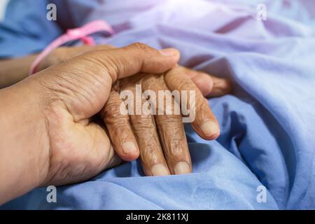Nahaufnahme eines Kindes, das die Hand der Mutter hält, während es krank ist, und die Hand des Sohnes berührt eine ältere Frau im Krankenhaus Stockfoto