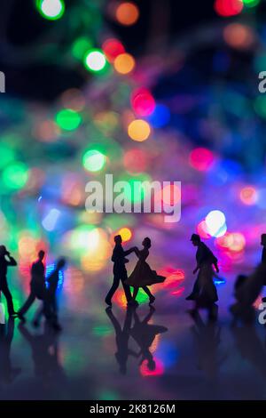 Miniatur-Spielzeug für Menschen - Ein Paar, das gemeinsam auf der Straße unter geschäftigen Pendlern tanzt, mit bunten Bokeh-Lichtern und Glücksgedanken. Stockfoto