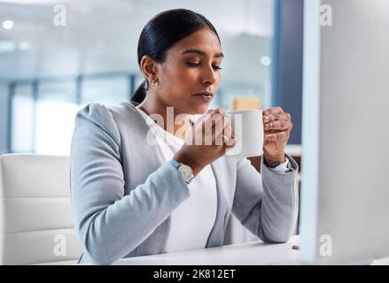 Hmm, ich brauchte diese Tasse Kaffee. Eine attraktive junge Geschäftsfrau, die allein im Büro saß und eine Tasse Kaffee genoss. Stockfoto