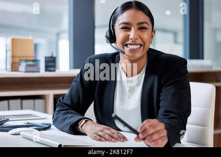 Es gibt kein Problem, das ich nicht lösen kann: Eine attraktive junge Geschäftsfrau, die allein in ihrem Büro sitzt und ein Headset trägt. Stockfoto