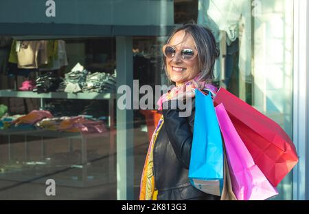 Dame mit Einkaufstaschen lächelt fröhlich und schaut vor einem Geschäft zur Kamera. Weihnachtseinkäufe. Stockfoto