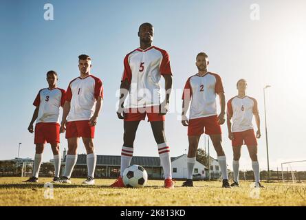 Fußballspieler, Teams und Sporttraining auf dem Fußballplatz durch Männer, die mit Ball, Kraft und starker Denkweise stehen. Fußball, Fitness und Mannfußball Stockfoto
