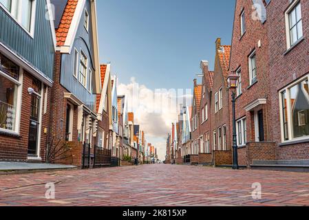 Blick auf die gepflasterte Straße und die typischen Gebäude in der niederländischen Stadt Volendam gegen den blauen Himmel Stockfoto