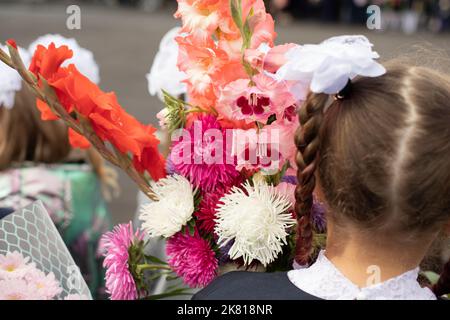 Kinder am Tag des Wissens. Die Erstklässler gehen zur Schule. Kinder mit Blumen für Lehrer. Details zum Schulurlaub. Stockfoto