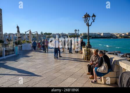 Touristen, die bei strahlendem Nachmittagssonne entlang der Uferpromenade von Otranto auf der Lungomare degli Eroi (die Heldenpromenade) spazieren. Apulien (Apulien), Italien. Stockfoto