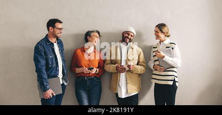 Eine Gruppe glücklicher Geschäftsleute, die fröhlich lächeln und auf ein Interview warten. Kandidaten in der engeren Auswahl mit verschiedenen digitalen Geräten Stockfoto