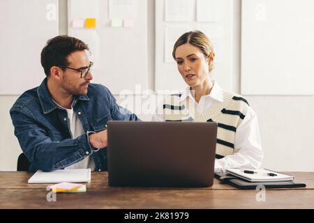 Zwei junge Geschäftsleute, die in einem kreativen Büro mit einem Laptop arbeiten, diskutieren. Zwei Geschäftsleute, die an einem neuen Projekt in einem zusammenarbeiten Stockfoto