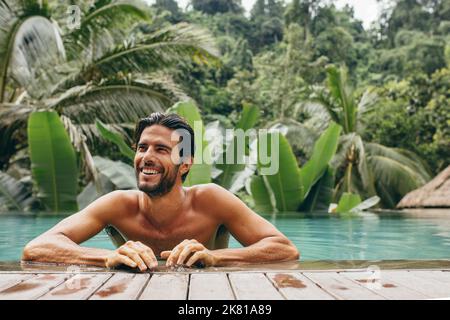 Porträt eines lächelnden jungen Mannes im Schwimmbad. Ein hübscher Mann im Pool sieht glücklich aus. Männer entspannen sich in einem luxuriösen Urlaubsort. Stockfoto