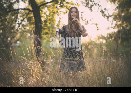 Hübsches Mädchen mit Vintage-Kamera zu Fuß durch Rasen im Wald Stockfoto