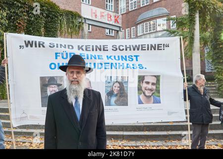 20. Oktober 2022, Hamburg: Shlomo Bistrizky, Staatsrabbiner von Hamburg, steht vor einem Transparent vor dem Eingang der Kunstschule bei einem Protest Hamburger Juden gegen die Ernennung von zwei ruangrupa-Gastprofessoren an der Hochschule für bildende Künste (HBFK). Teilnehmer im Hintergrund halten das Transparent mit der Aufschrift „Wir sind keine Schweine!“ Für eine Kunst ohne Judenhass.'. Die Gastprofessoren sind Mitglieder des indonesischen documenta-Kuratorenkollektivs ruangrupa. Die Ausgabe 15. der Kunstausstellung war von immer neuen Anschuldigungen des Antisemitismus überschattet worden. Foto: Georg Stockfoto