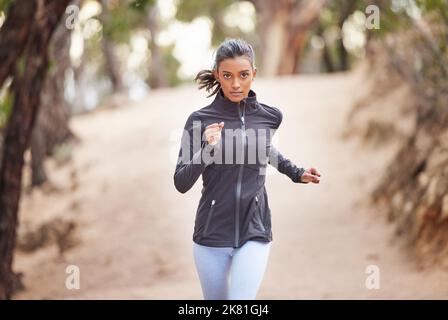 Eine junge Frau, die durch einen Wald joggt. Stockfoto