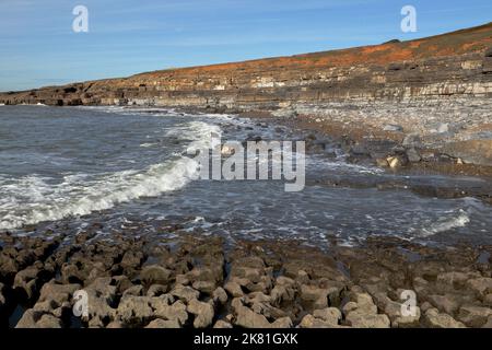 Eine große Bucht in der Nähe des bekannten Ogmore vertieft sich, zeigt Felsschichten und riesige zufällige Felsen mit der Flut auf dem Weg in. Stockfoto