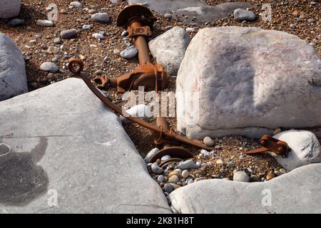 Zertrümmerte und zerbrochene Hinterachse, die zwischen Felsen festsitzt und teilweise in einer kleinen Bucht entlang der Küste vergraben ist. Stockfoto