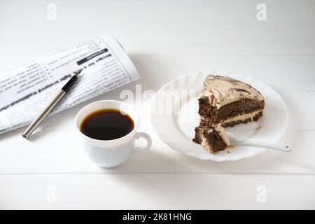 Businessman-Frühstück. Auf dem Tisch eine Tasse Kaffee, ein Stück Kuchen, eine Zeitung und ein Stift Stockfoto