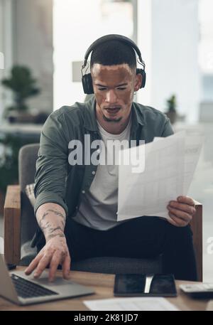 Wir müssen zuerst glauben, dass wir Erfolg haben können, ein junger Geschäftsmann, der Kopfhörer bei der Arbeit verwendet. Stockfoto