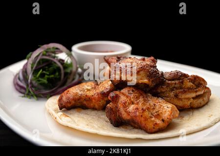 Schweinekebab mit Grillsoße auf einem Teller, auf schwarzem Hintergrund, mit verschwommenem Hintergrund Stockfoto
