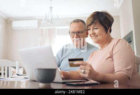 Unsere Bank sorgt dafür, dass wir Geld sparen. Ein reifes Paar, das seine Bankkarte nutzt, um seine Rechnungen digital zu bezahlen. Stockfoto