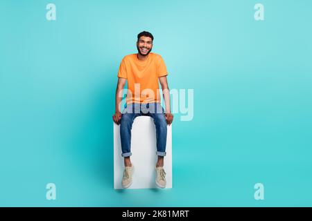Ganzkörper-Foto von zufrieden froh junge Person sitzen Podium isoliert auf aquamarinfarbenem Hintergrund Stockfoto