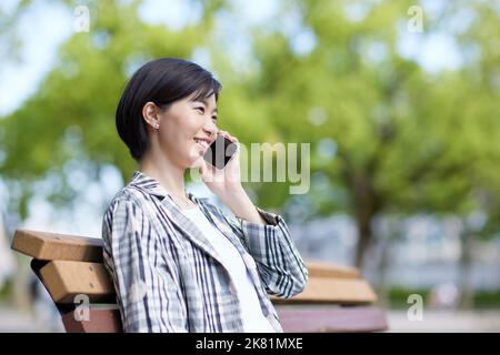 Junge Japanerin mit Smartphone in einem Stadtpark Stockfoto