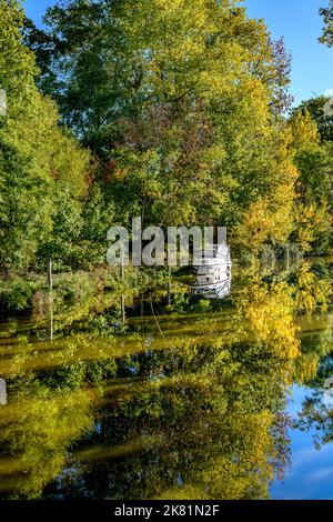 Herbstspiegelungen bei einer sanften Kurve auf dem River Medway in Tonbridge, Kent, Großbritannien. Mitten in der Szene befindet sich ein kleines Motorboot. Stockfoto