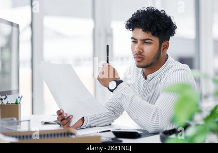 Ein Blick über ein paar Geschäftsberichte. Ein junger Geschäftsmann, der in einem Büro Papierkram durchläuft. Stockfoto