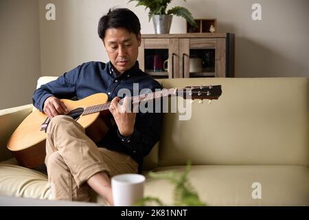 Japanischer Mann spielt akustische Gitarre Stockfoto