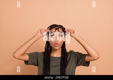 Portrait von beeindruckt überrascht Mädchen Hände berühren Brillen schauen interessiert leeren Raum isoliert auf beige Farbe Hintergrund Stockfoto