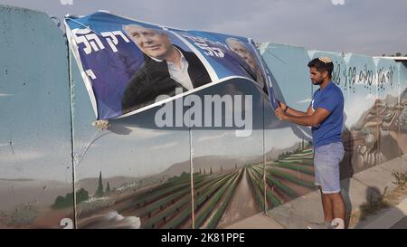 HAWARA, WESTJORDANLAND - 19. OKTOBER: Ein Israeli hängt ein Wahlkampfbanner für die Likud-Partei, auf dem ihr Anführer Benjamin Netanjahu in einer bemalten Stahlbetonbetonbetonwand gegen das Scharfschützenfeuer am 19. Oktober 2022 in der Nähe der palästinensischen Stadt Hawara, südlich von Nablus, Westjordanland, abgebildet ist. Weniger als zwei Wochen vor Israels fünfter Wahl in vier Jahren, inmitten der eskalierenden Gewalt im Westjordanland, prognostiziert die Umfrage eine niedrige israelische arabische Wahlbeteiligung, die Benjamin Netanjahu und der extremen Rechten eine parlamentarische Mehrheit den Weg ebnen kann. Kredit: Eddie Gerald/Alamy Live Nachrichten Stockfoto