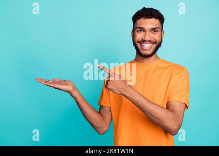 Foto von ziemlich positiven Kerl tragen orange T-Shirt zeigen Finger Arm leeren Raum isoliert blaugrün Hintergrund Stockfoto