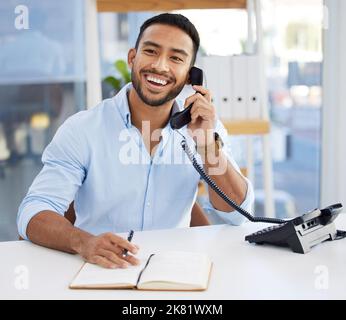 Wenn ein Unternehmen anruft, antworte ich. Ein junger Geschäftsmann schreibt in einem Notebook, während er das Telefon bei der Arbeit benutzt. Stockfoto