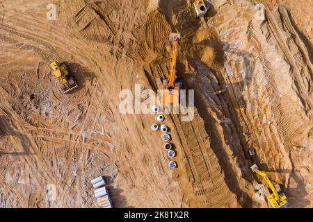 Auf der Baustelle gräbt ein Bagger Graben, um Kanalleitungen zu verlegen und unterirdische Regenwasserkanäle zu verbinden Stockfoto