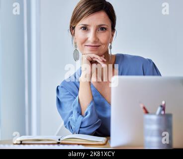 Hier soll ich sein: Eine junge Geschäftsfrau, die ihren Laptop bei der Arbeit benutzt. Stockfoto