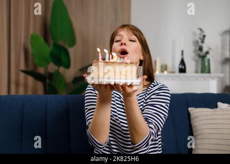 Alles gute zum Geburtstag. Junge Frau bläst Kerzen auf einem Geburtstagskuchen aus Stockfoto