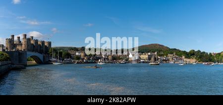 Conwy, Vereinigtes Königreich - 27. August 2022: Panoramablick auf das Conwy Castle und die Brücke mit der ummauerten Stadt und dem Hafen dahinter Stockfoto