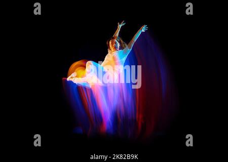 Im Wunderflug. Junge sportliche Tänzerin in weißen Kleidern schweben, bewegen sich über dunklen Hintergrund in gemischtem Neonlicht. Kreative Kunst, Aspiration, Musik Stockfoto